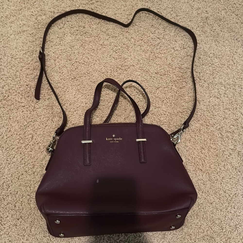 Maroon Kate Spade purse. Small white spot on the front. Has cross body strap.